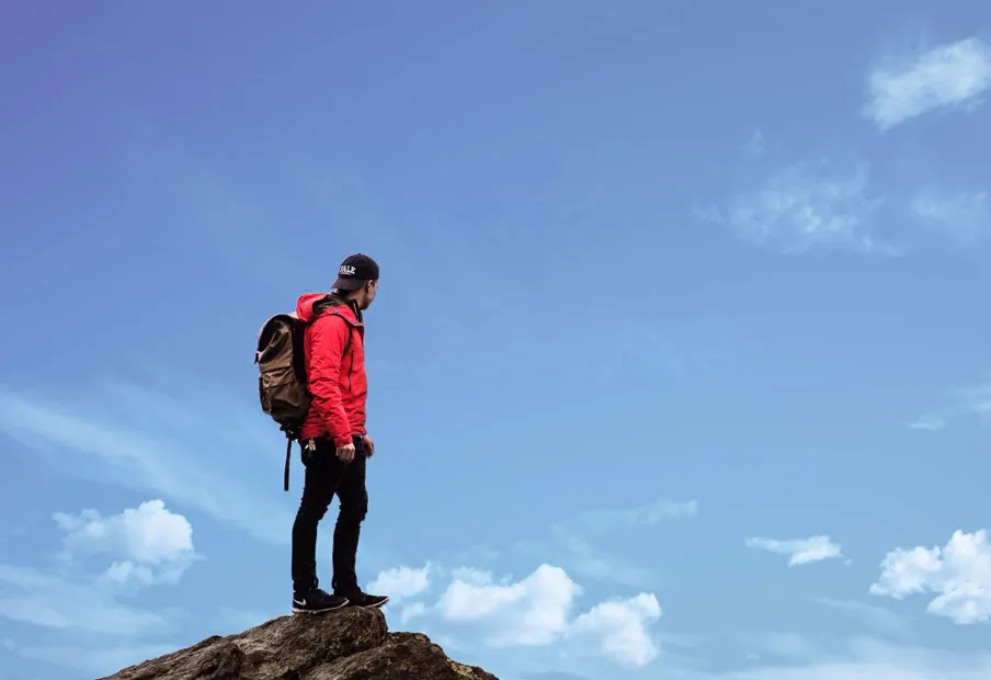 Hiker in a red jacket standing on a rocky outcrop above the clouds