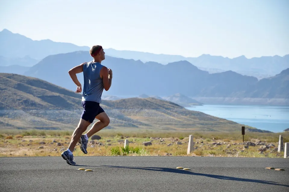 Runner on an open road with mountains and a lake behind him